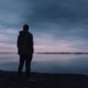 Man in grief stands looking out at water.