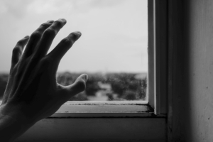 A black and white photo of a grieving person is touching the glass of a window, with only their hand visible